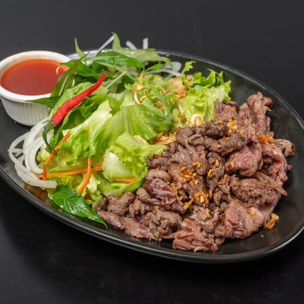 Vietnamese beef salad with lettuce, herbs, onions, and a side of red chili sauce.