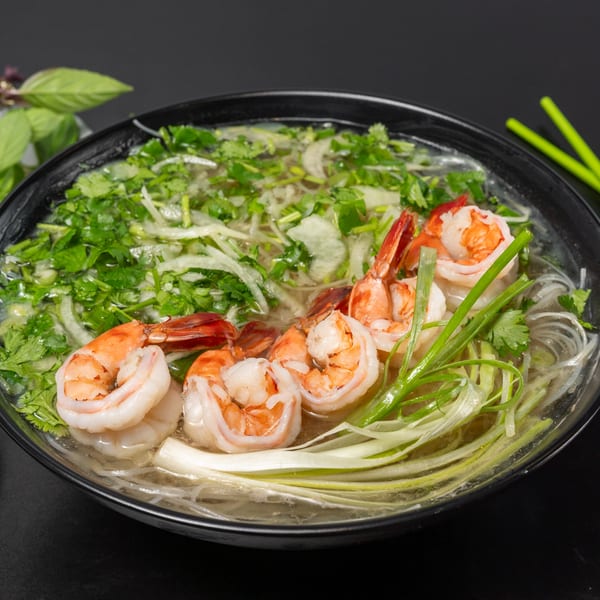 Close-up of Pho Tick Tock's shrimp pho with noodles, herbs, and green onions in a black bowl.