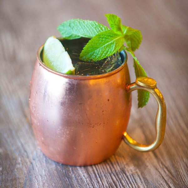 A copper mug filled with a dark drink, ice, a lime wedge, and fresh mint sprigs.