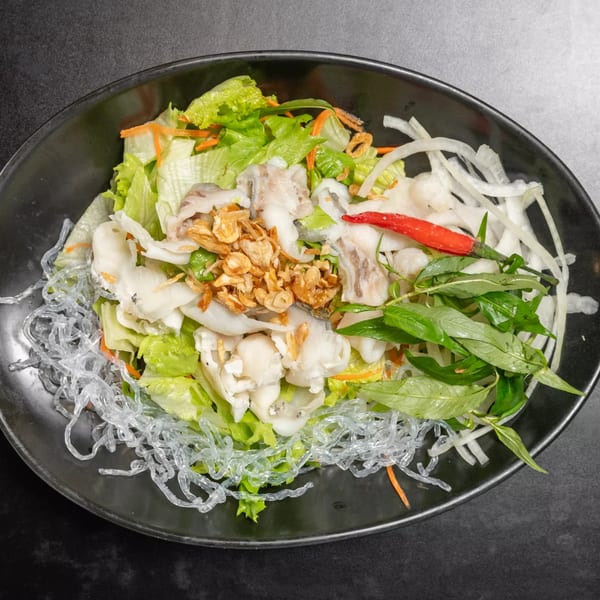 Vietnamese salad with white fish, glass noodles, lettuce, herbs, and a red chili in a black bowl.