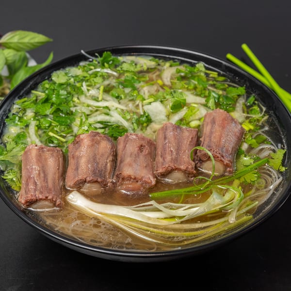 A close-up of Pho Tick Tock's pho with five large pieces of beef, noodles, and fresh herbs.