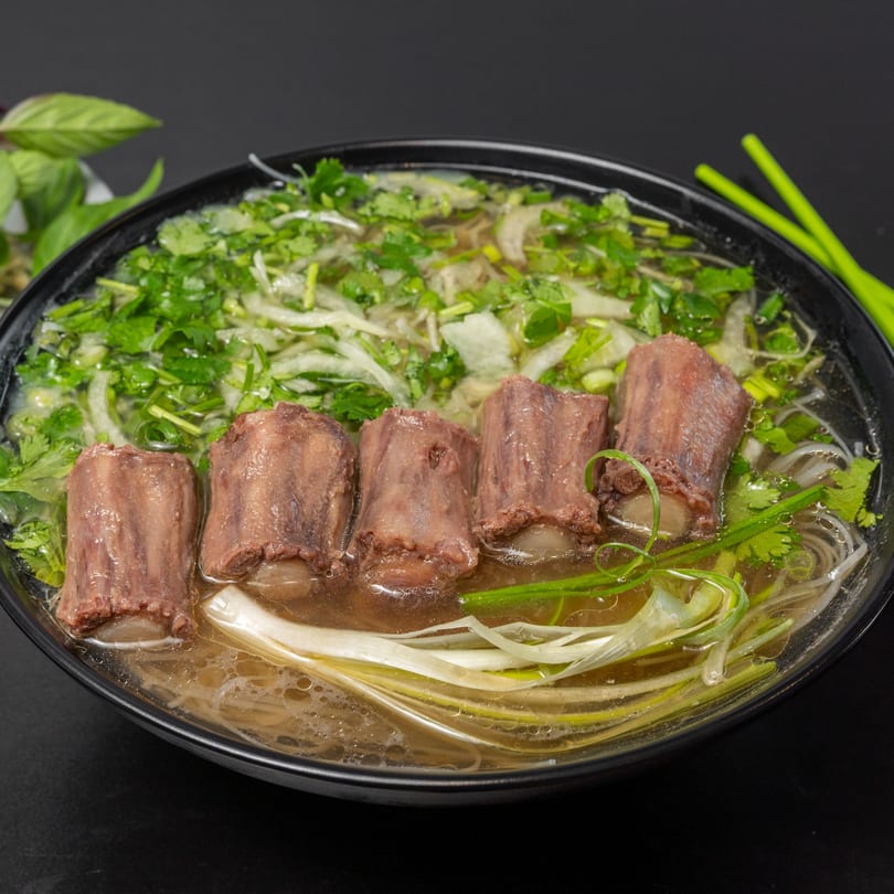 A close-up of Pho Tick Tock's pho with five large pieces of beef, noodles, and fresh herbs.