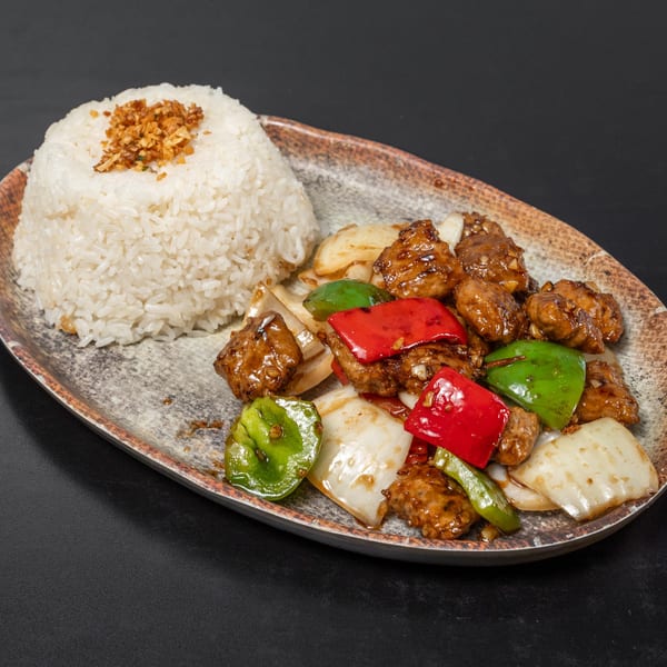 Vietnamese dish with rice, glazed meat, red and green bell peppers, and onions on a plate.