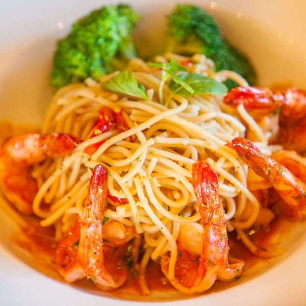 Spaghetti with shrimp, red peppers, and basil, garnished with broccoli florets in a white bowl.