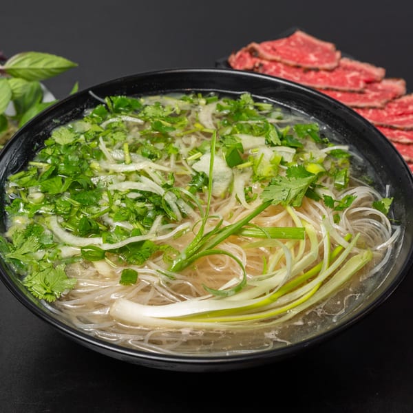 Pho Tick Tock's pho with noodles, herbs, and thinly sliced beef on a dark background.