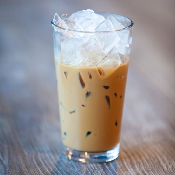A tall glass of Vietnamese iced coffee with ice cubes on a wooden table.