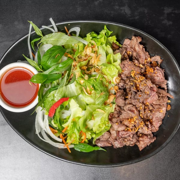 Vietnamese beef salad with lettuce, herbs, fried onions, and a side of red sauce.