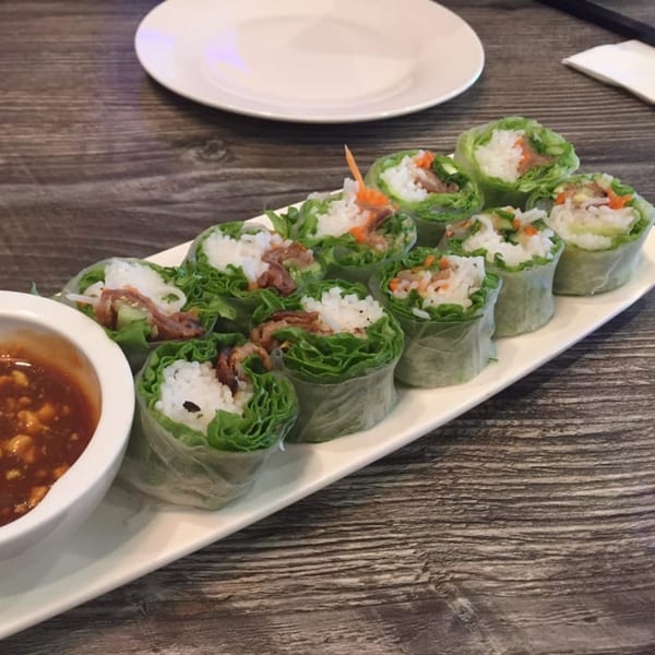 A long white plate of fresh Vietnamese spring rolls with peanut dipping sauce on a wooden table.