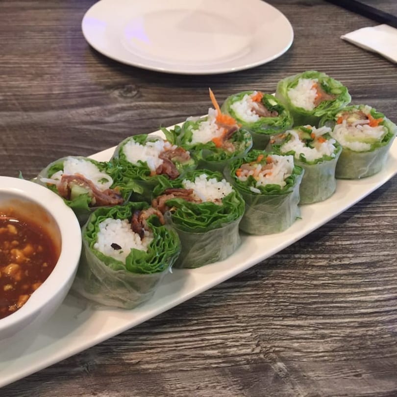 A long white plate of fresh Vietnamese spring rolls with peanut dipping sauce on a wooden table.
